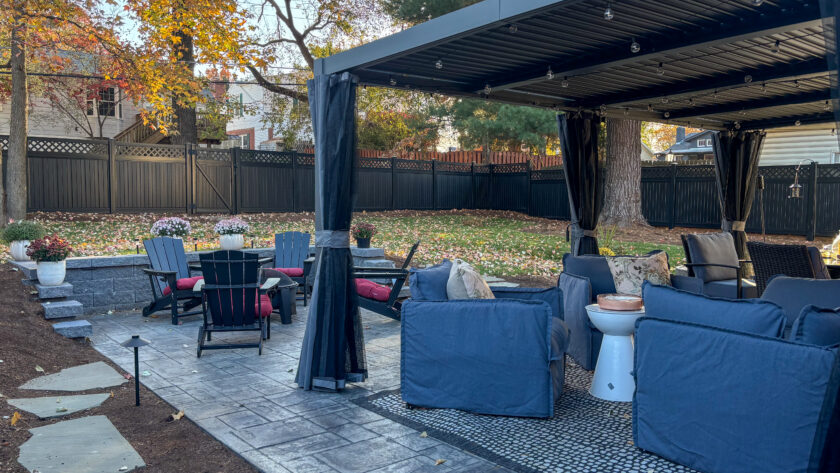 Outdoor patio area with blue cushioned seating under a canopy, string lights, and autumn leaves scattered on the ground.