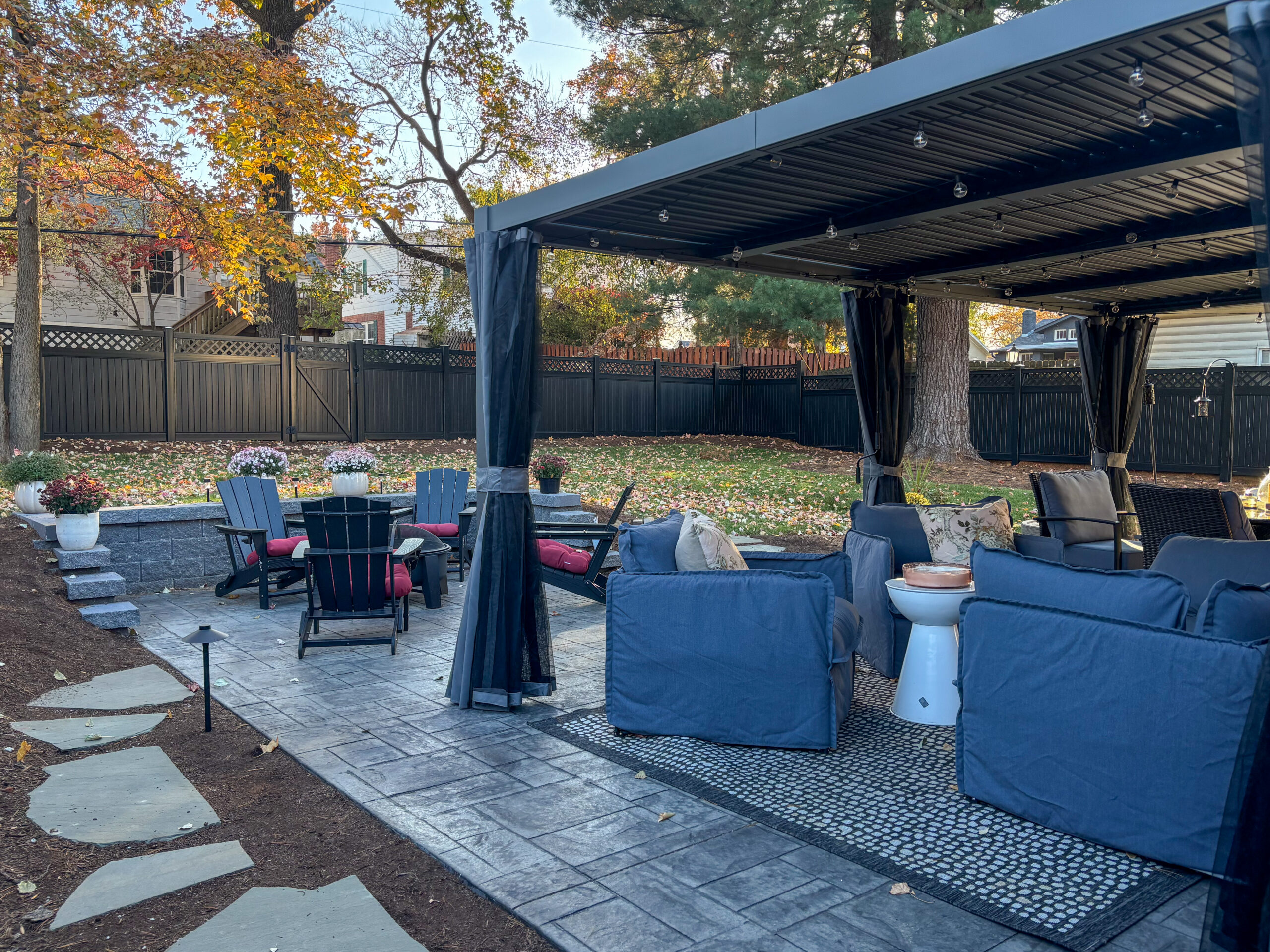 Outdoor patio area with blue cushioned seating under a canopy, string lights, and autumn leaves scattered on the ground.