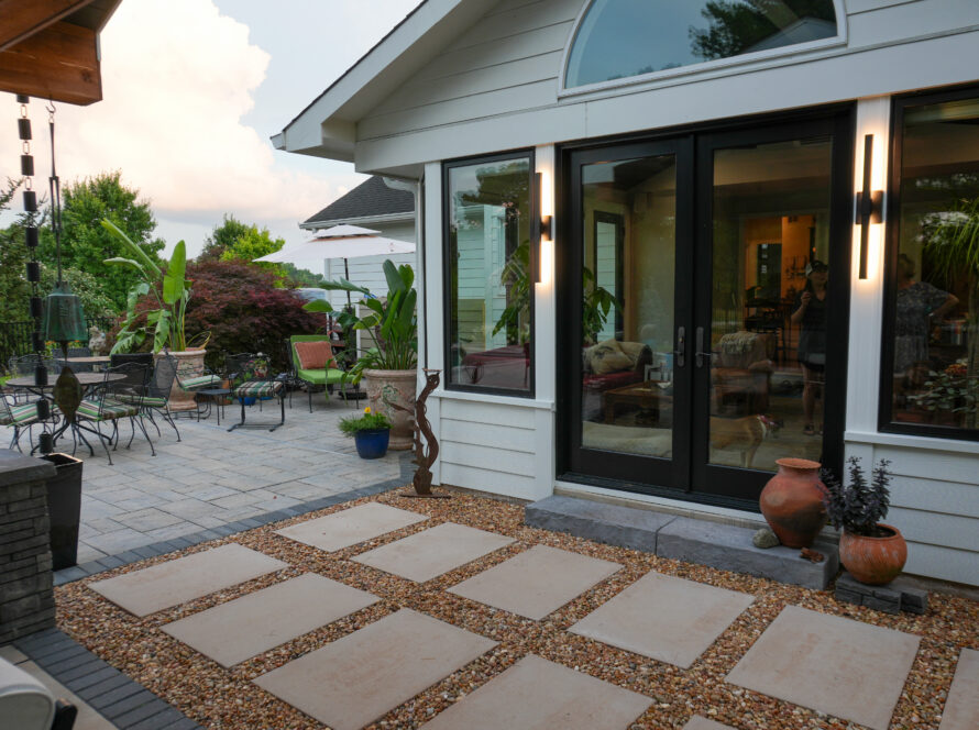 Patio with beige stepping stones, gravel, and outdoor dining set beside glass doors leading into a house.
