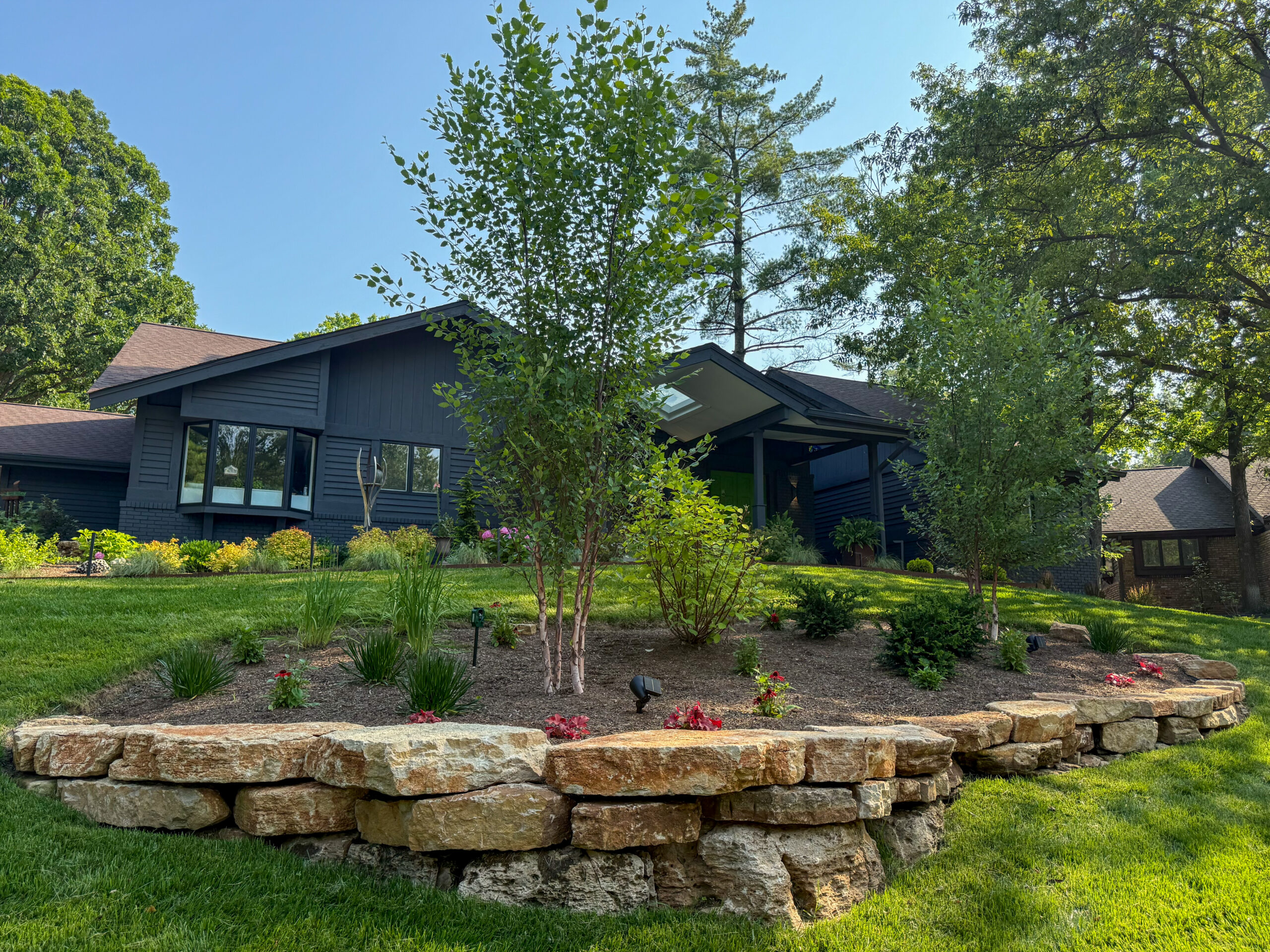 After: tiered stone wall with planted terraces, same camera position
