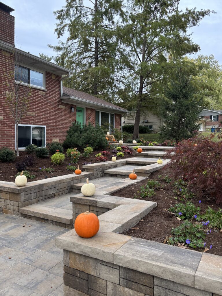 Brick house with a green front door, stone stepped planters, and pumpkins scattered along the front steps for autumn decor.
