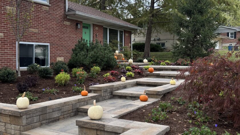 Brick house with a green front door, stone stepped planters, and pumpkins scattered along the front steps for autumn decor.