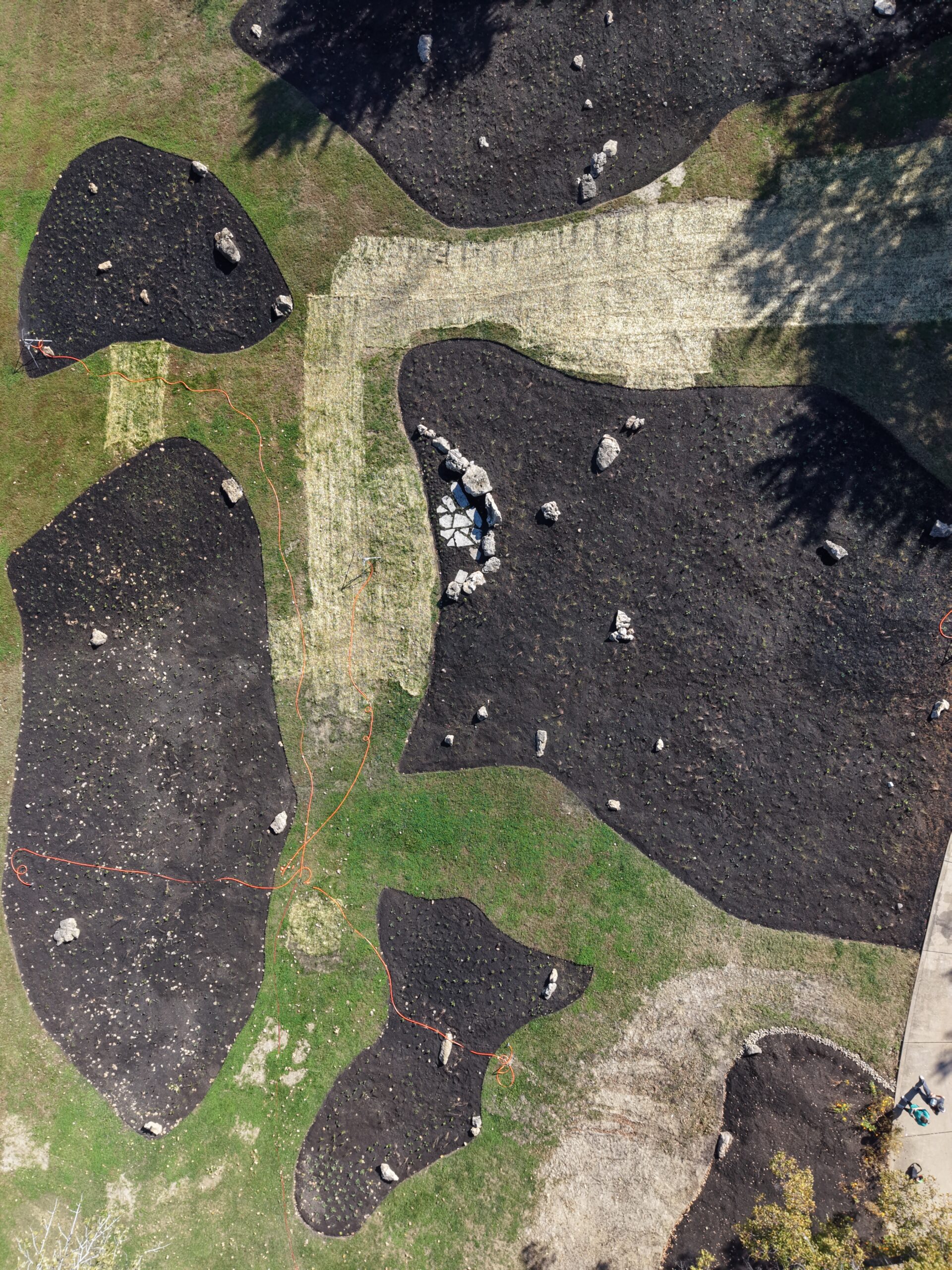 default | Quiet Village Landscaping Aerial view of a landscape with irregular dark mulch islands separated by beige gravel paths and scattered rocks.